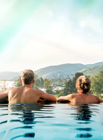 Gäste entspannen im Infinity Pool mit Blick über Stein und die Donau und die Wachau
